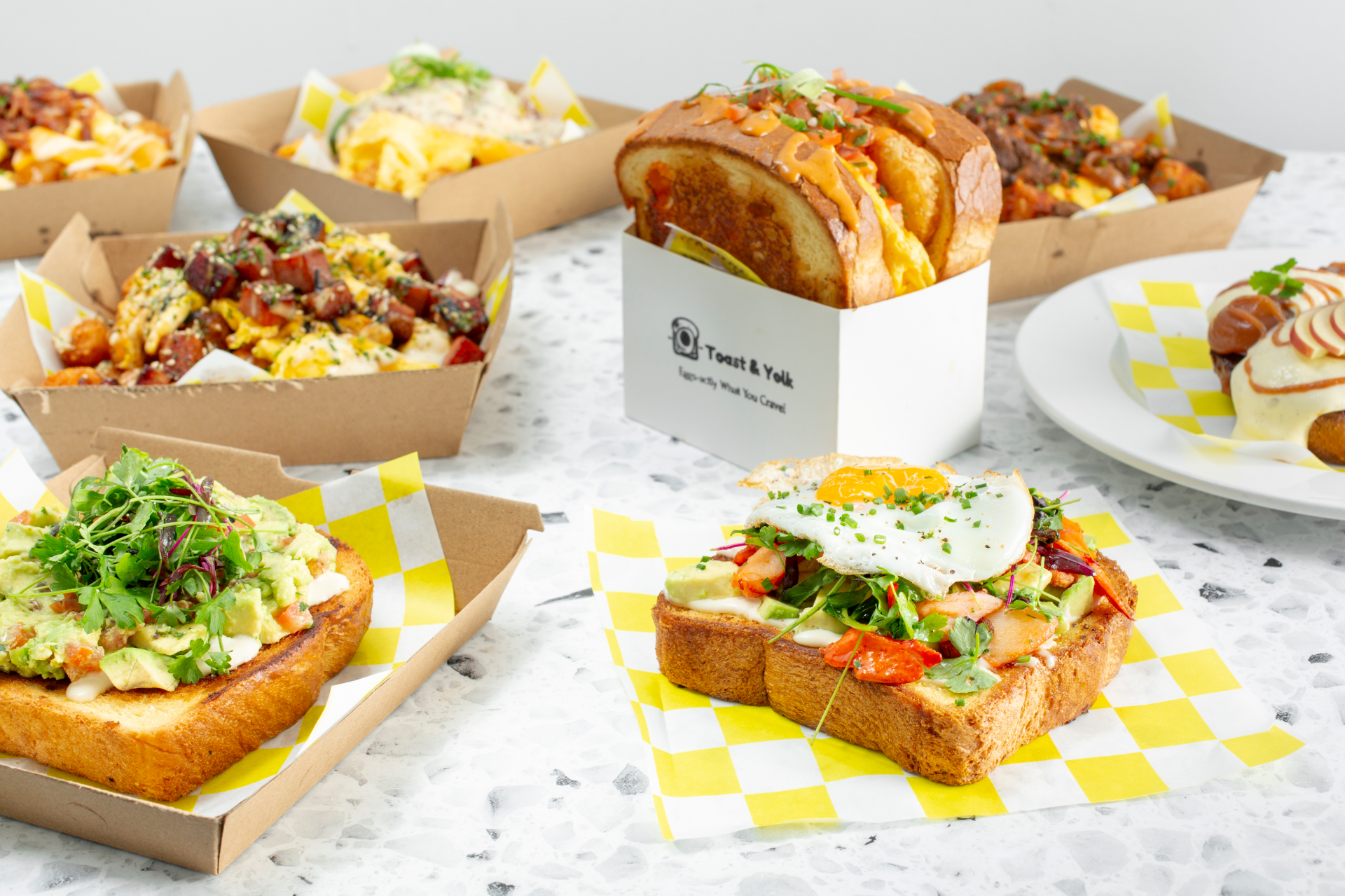Toast & Yolk full spread — sandwiches, tots, and bowls served on signature yellow checkered paper